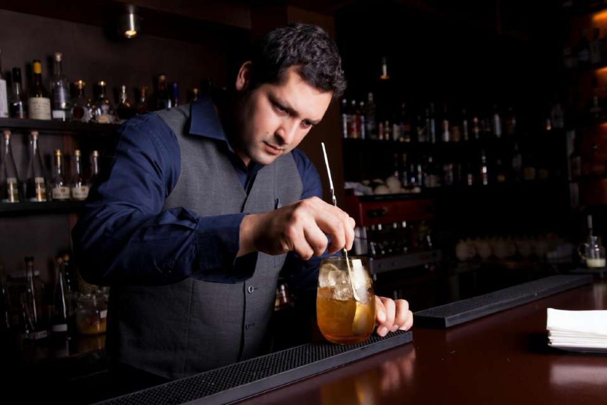 Barmen bar tezgâhında kokteyl karıştırıyor